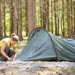 Person baut im Naturpark Neckartal-Odenwald ein grünes Trekkingzelt auf einem moosigen Waldboden zwischen hohen Fichten auf.