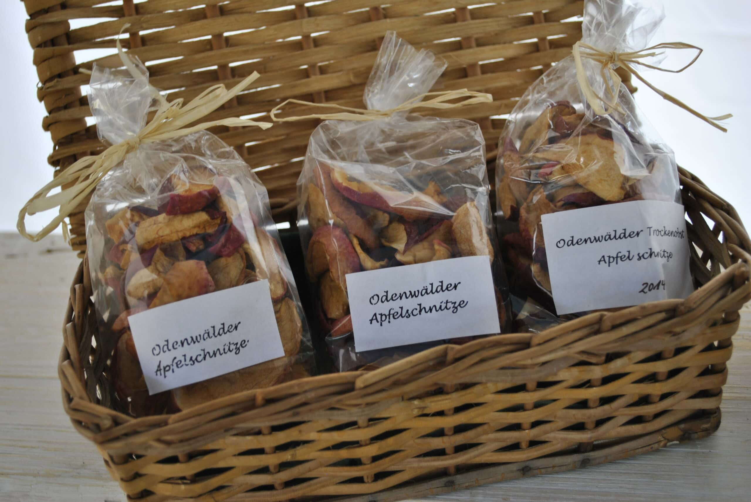 Drei durchsichtige Beutel mit getrockneten Odenwälder Apfelschnitten in einem geflochtenen Korb, jeweils mit Beschriftung.