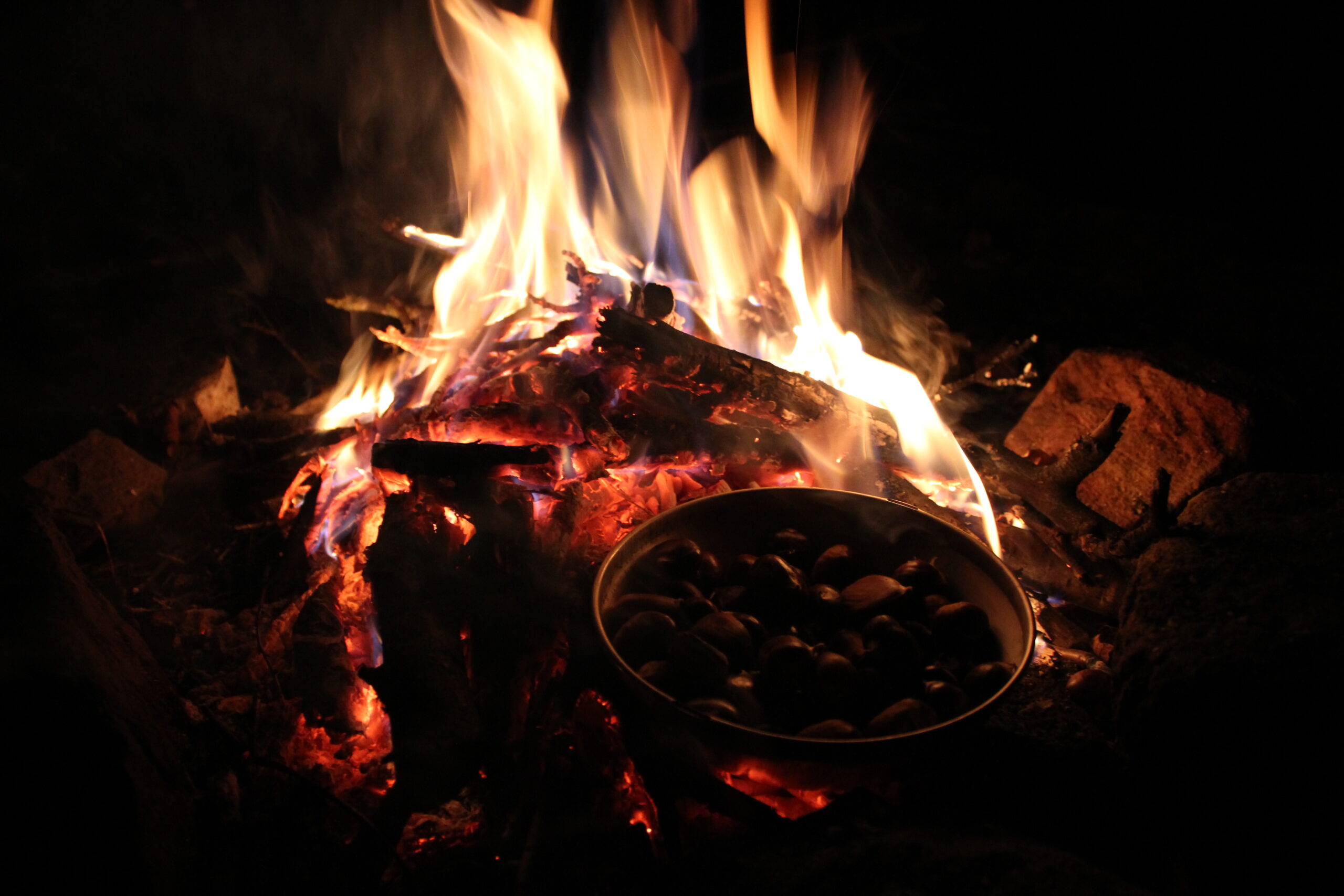 Lagerfeuer mit glühenden Holzscheiten und daneben ein Metalltopf über den Flammen, typisch fürs Zelten im Naturpark Neckartal-Odenwald.