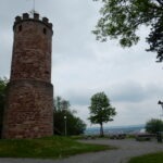 Steinerne Aussichtsplattform mit Flagge im Naturpark Neckartal-Odenwald, umgeben von Grünflächen und Bänken, mit Panoramablick über die Landschaft.