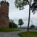 Historischer Aussichtsturm aus rotem Sandstein mit Aussichtsplattform, umgeben von Grünflächen und Bänken, mit Fernblick über das Neckartal-Odenwald.