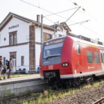Drei Personen mit Rucksäcken steigen am Bahnhof Auerbach aus einem roten Regionalzug Richtung Odenwald aus, umgeben von historischem Bahnhofsgebäude.