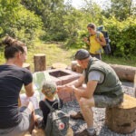Gruppe von Wanderern im Naturpark Neckartal-Odenwald, die auf Baumstumpfsitzen eine Wanderkarte studiert und sich auf der Route berät.