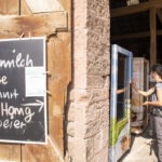 Person mit Rucksack bedient im Naturpark Neckartal-Odenwald eine Kühlbox mit regionalen Bio-Produkten wie Bio-Milch, Käse, Joghurt, Honig und Bio-Eiern.