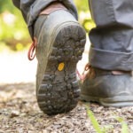 Wanderschuhe mit Profilsohle und Karabinerhaken auf Waldboden im Naturpark Neckartal-Odenwald, umgeben von Laub und Erde.