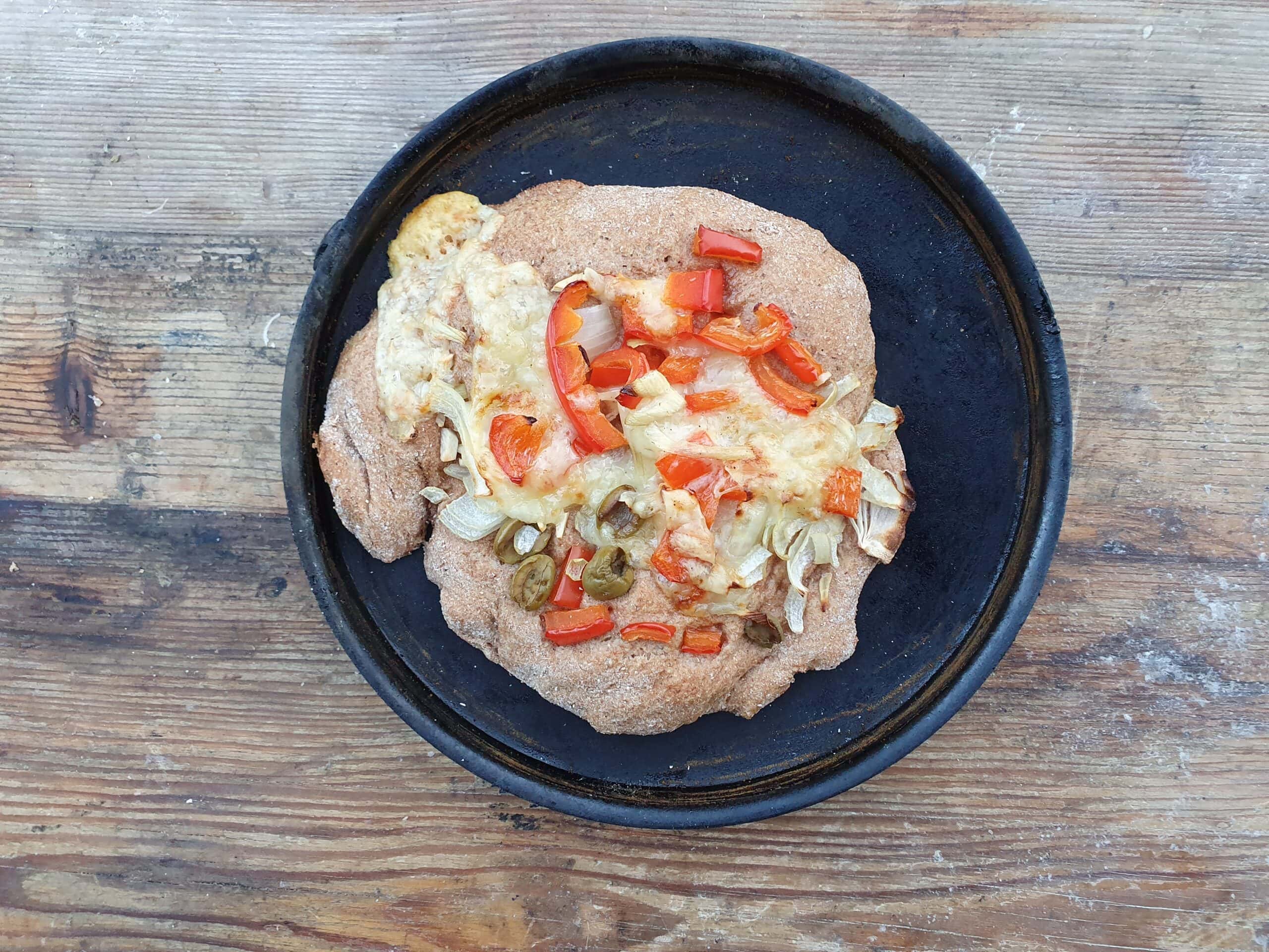 Gebratene Fladen mit Käse, Paprika und Zwiebeln auf einer schwarzen Pfanne, serviert auf einer rustikalen Holzoberfläche.
