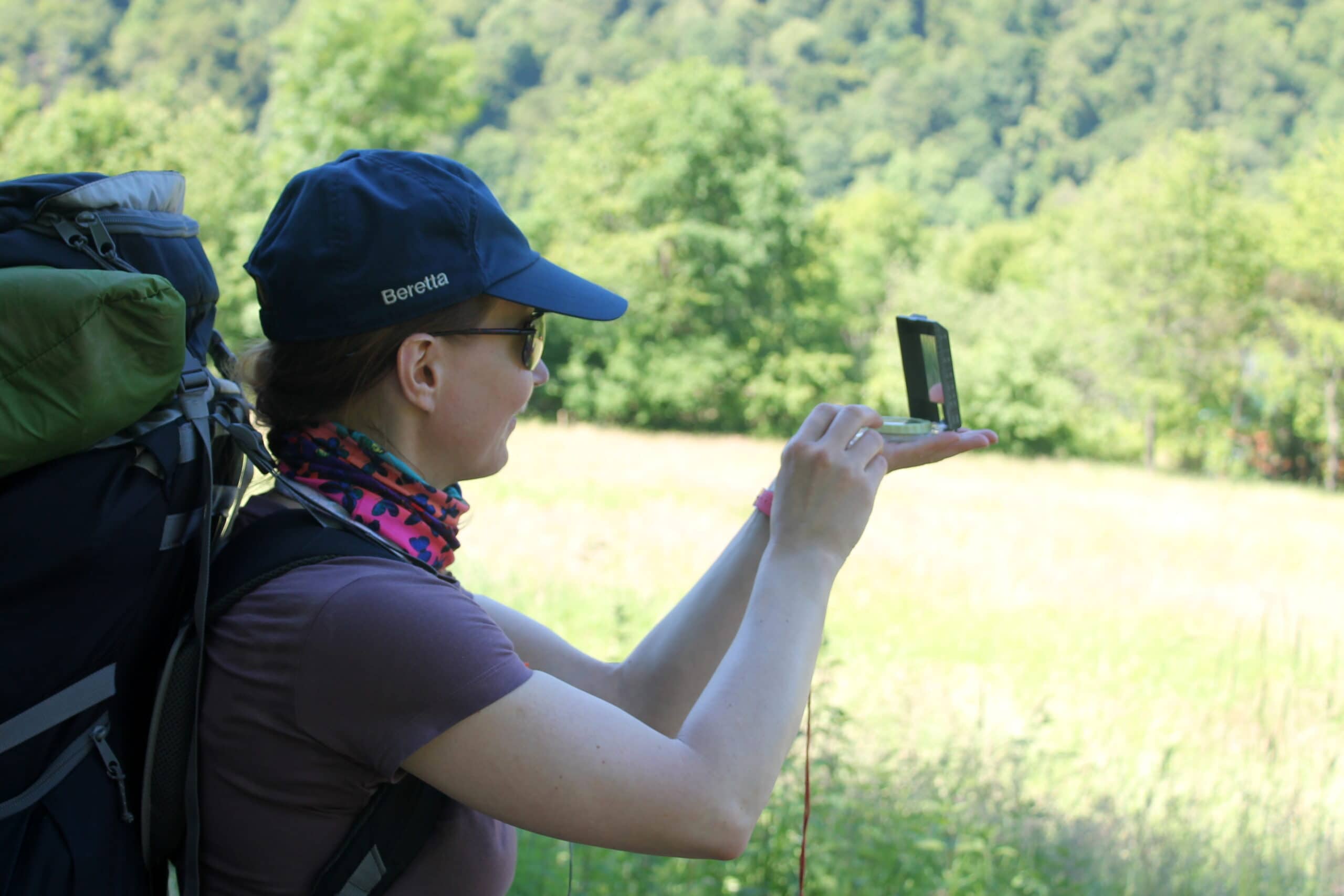 Person mit Rucksack nutzt GPS-Gerät zur Orientierung in der grünen Landschaft des Naturparks Neckartal-Odenwald während einer Wanderung.