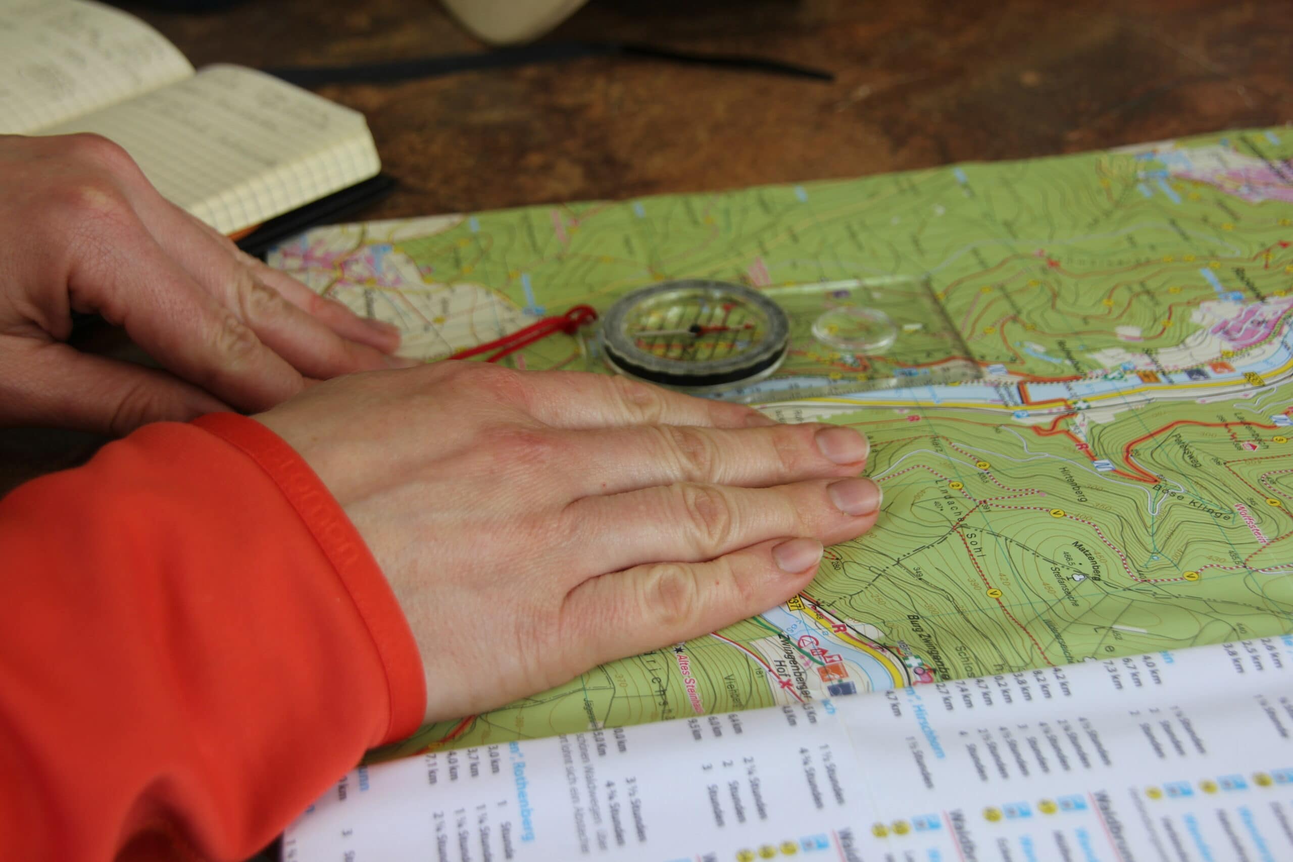 Person studiert Wanderkarte des Naturparks Neckartal-Odenwald mit Kompass zur Routenplanung für eine Trekking-Tour.